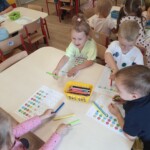 Dzieci przy stoliku uzupełniają kartę pracy.