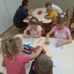 Dzieci przy stoliku uzupełniają kartę pracy.