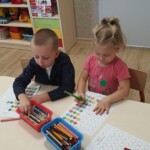 Dzieci przy stoliku uzupełniają kartę pracy.