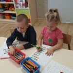 Dzieci przy stoliku uzupełniają kartę pracy.